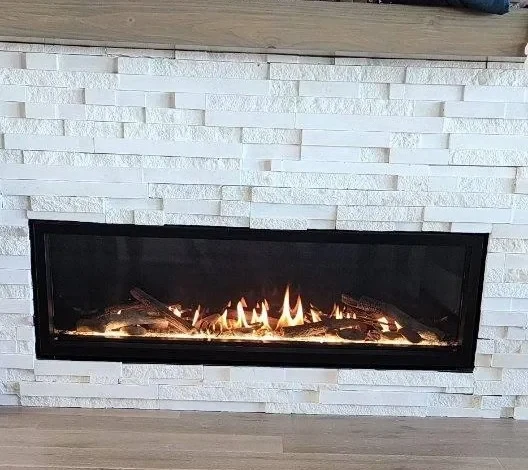 Linear gas fireplace with driftwood log set and white stacked-stone surround